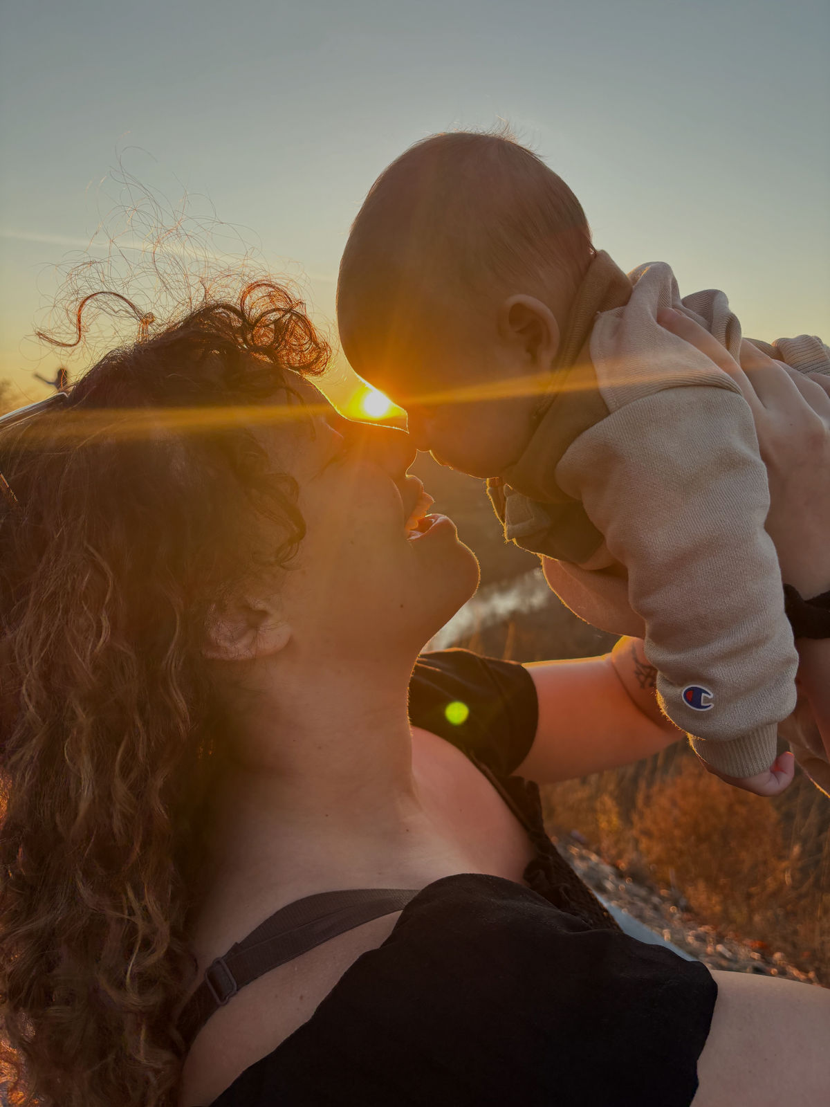 A mother lifts her baby nose-to-nose against a golden sunset